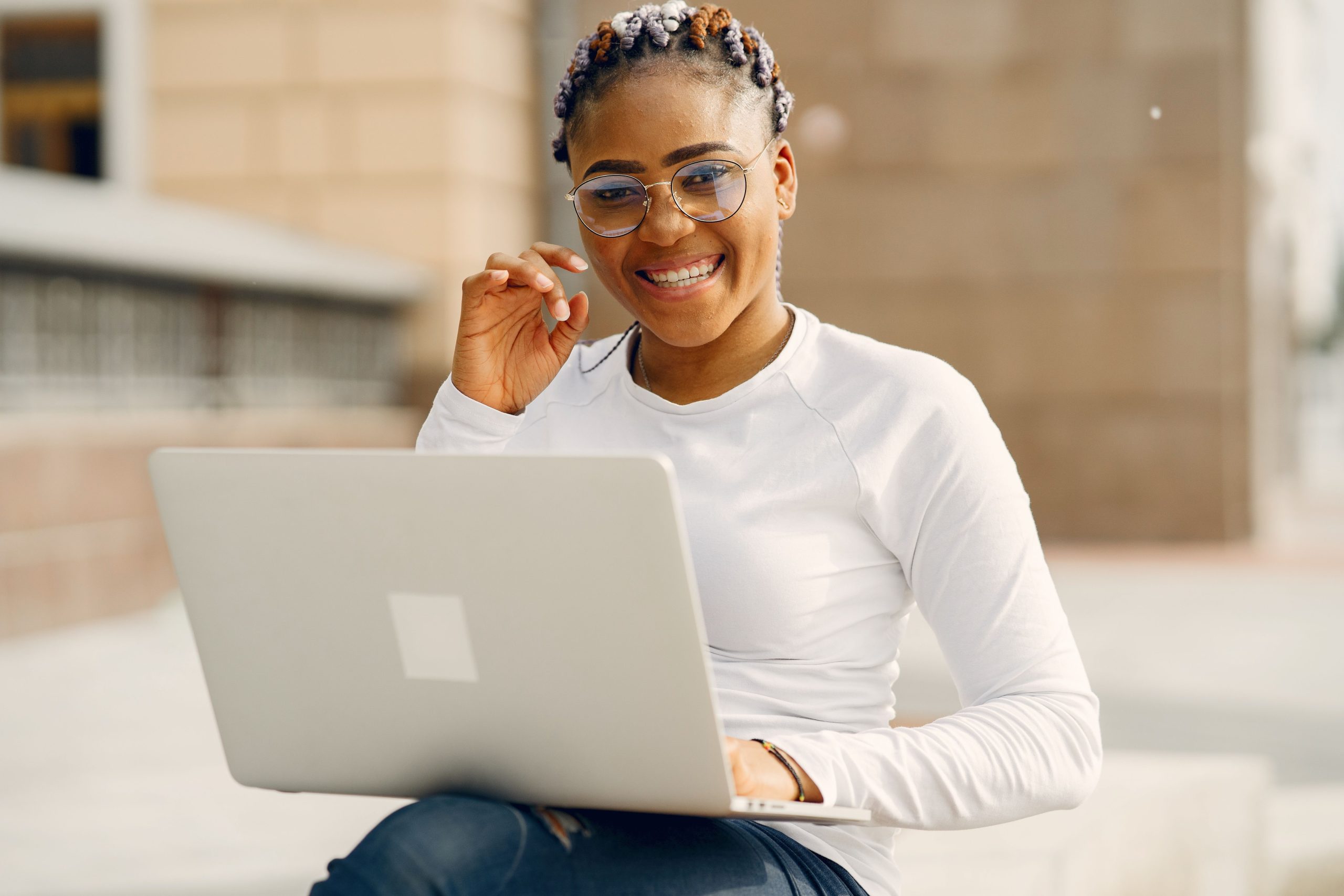 a woman sitting outside with a laptop smiling and waving at the camera